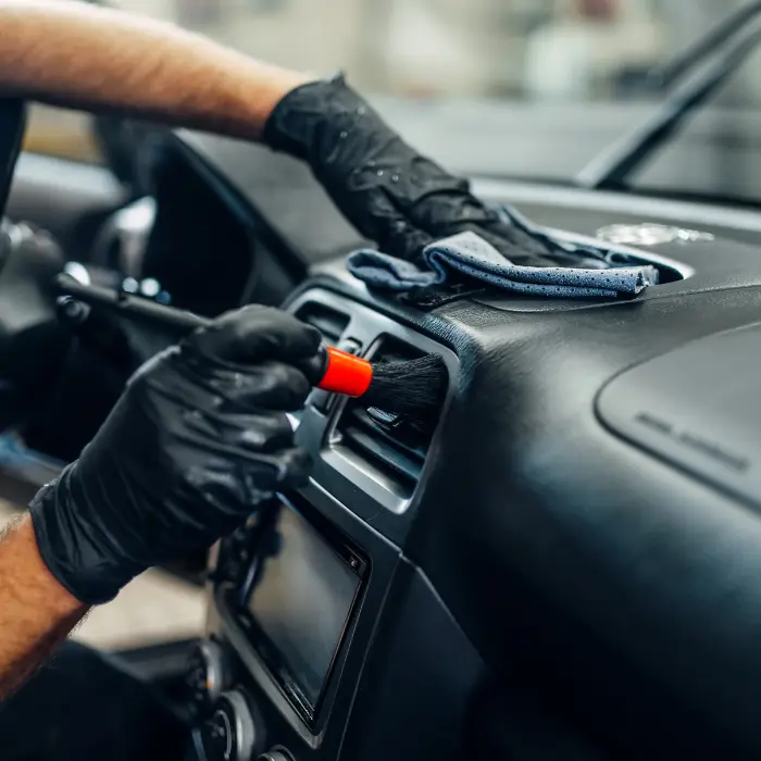 Nettoyage de véhicule détaillé des bouches d'aération de la voiture avec une brosse, soulignant le souci du détail et l'expertise du service de nettoyage intérieur de véhicule.