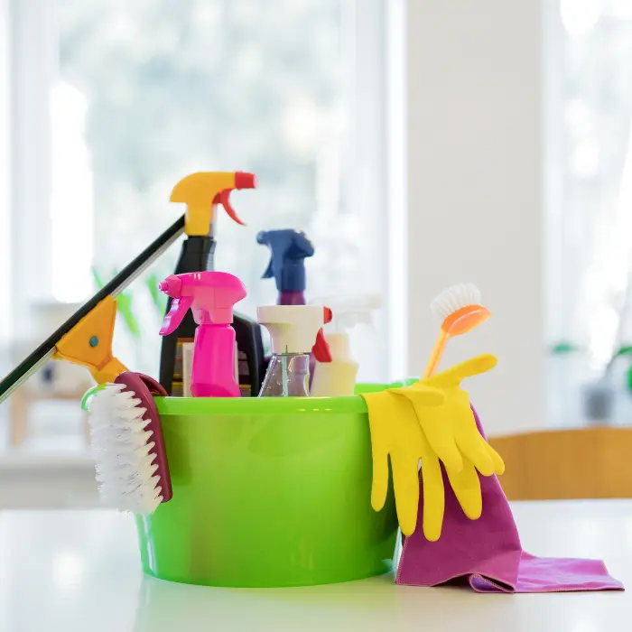 Seau vert vibrant rempli d'outils de nettoyage colorés, incluant des vaporisateurs, brosses, et gants en caoutchouc, prêts pour le service de nettoyage quotidien d'ISL Nettoyage.