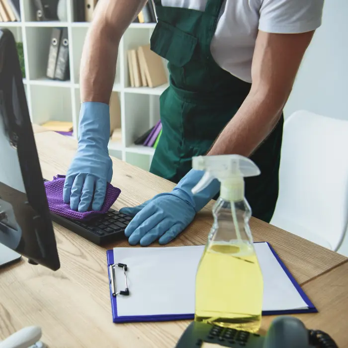 Professionnel en tenue de nettoyage désinfectant un clavier d'ordinateur avec attention, représentant le service méticuleux de nettoyage quotidien de bureaux d'ISL Nettoyage.