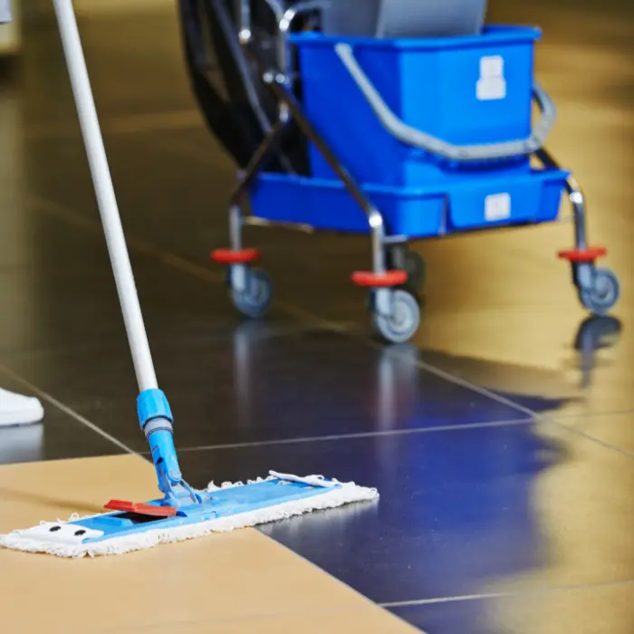 Nettoyage efficace d'un sol brillant avec un balai à franges bleu et blanc et un chariot de nettoyage, illustrant le service de nettoyage de sols commerciaux par ISL Nettoyage.